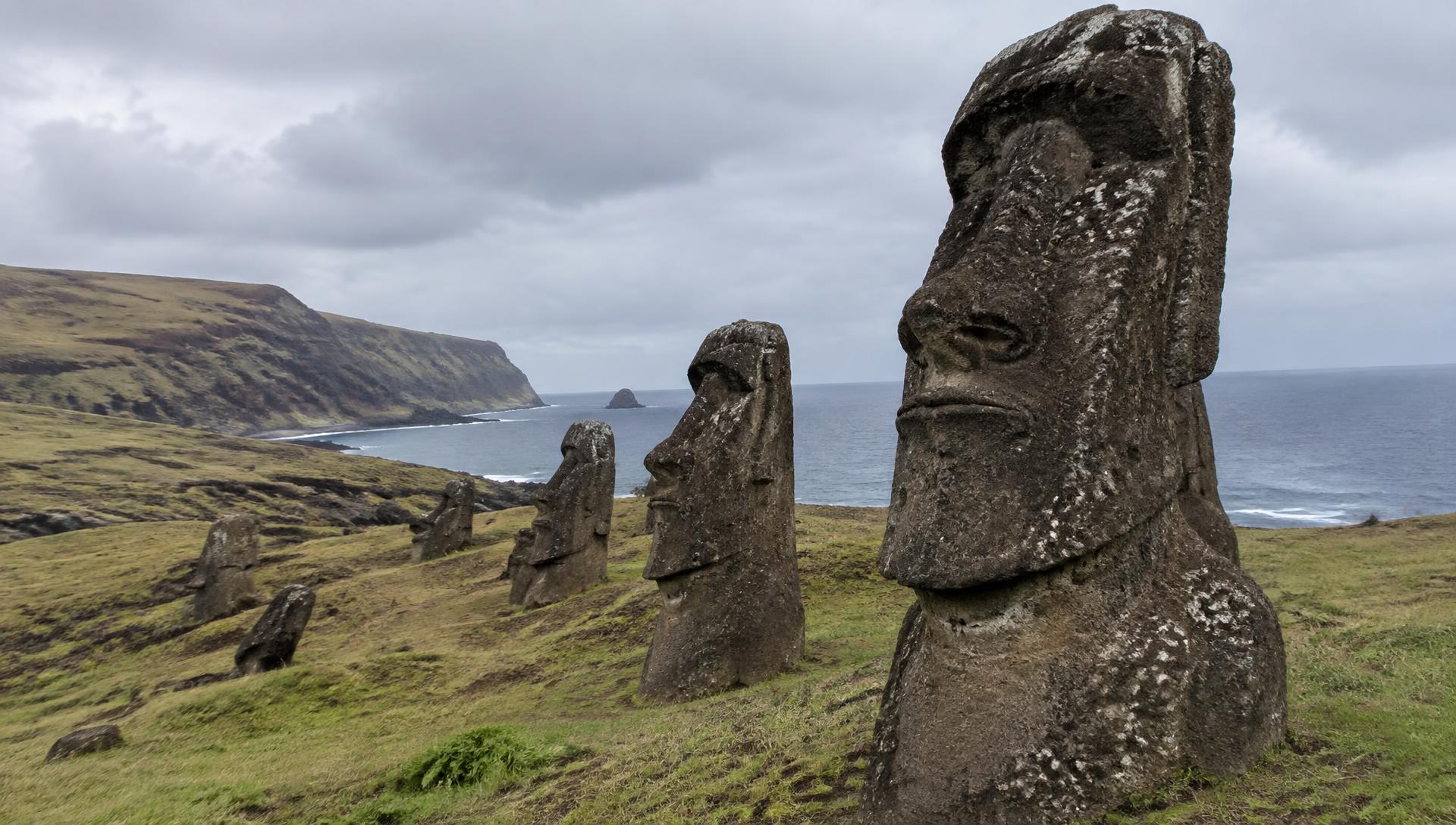 Mehrere Moai-Statuen auf einem grasbewachsenen Vulkanhang mit Pazifik im Hintergrund